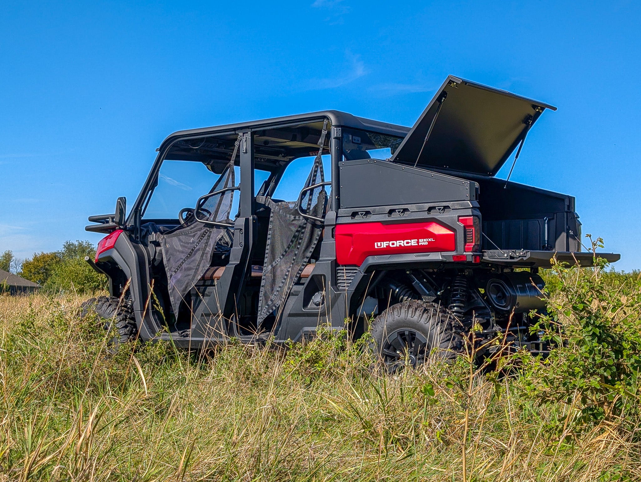 Red UTV with open cargo box in a grassy field under a clear blue sky