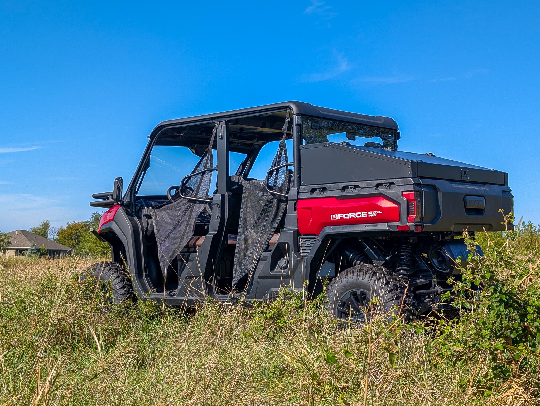 Black and red CF Moto off-road vehicle with a storage box in a grassy field with a clear blue sky.