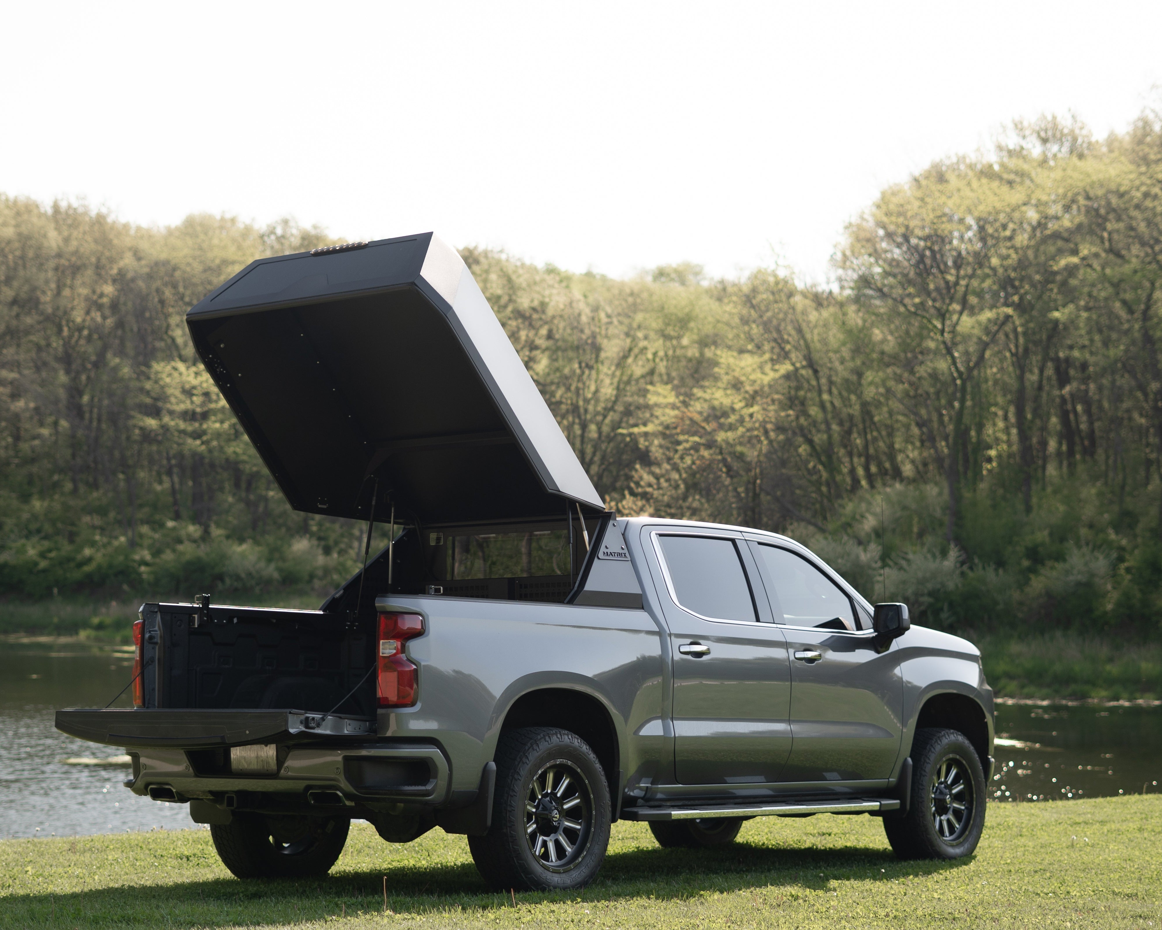 Silver pickup truck with an open cargo bed by a lake with trees in the background